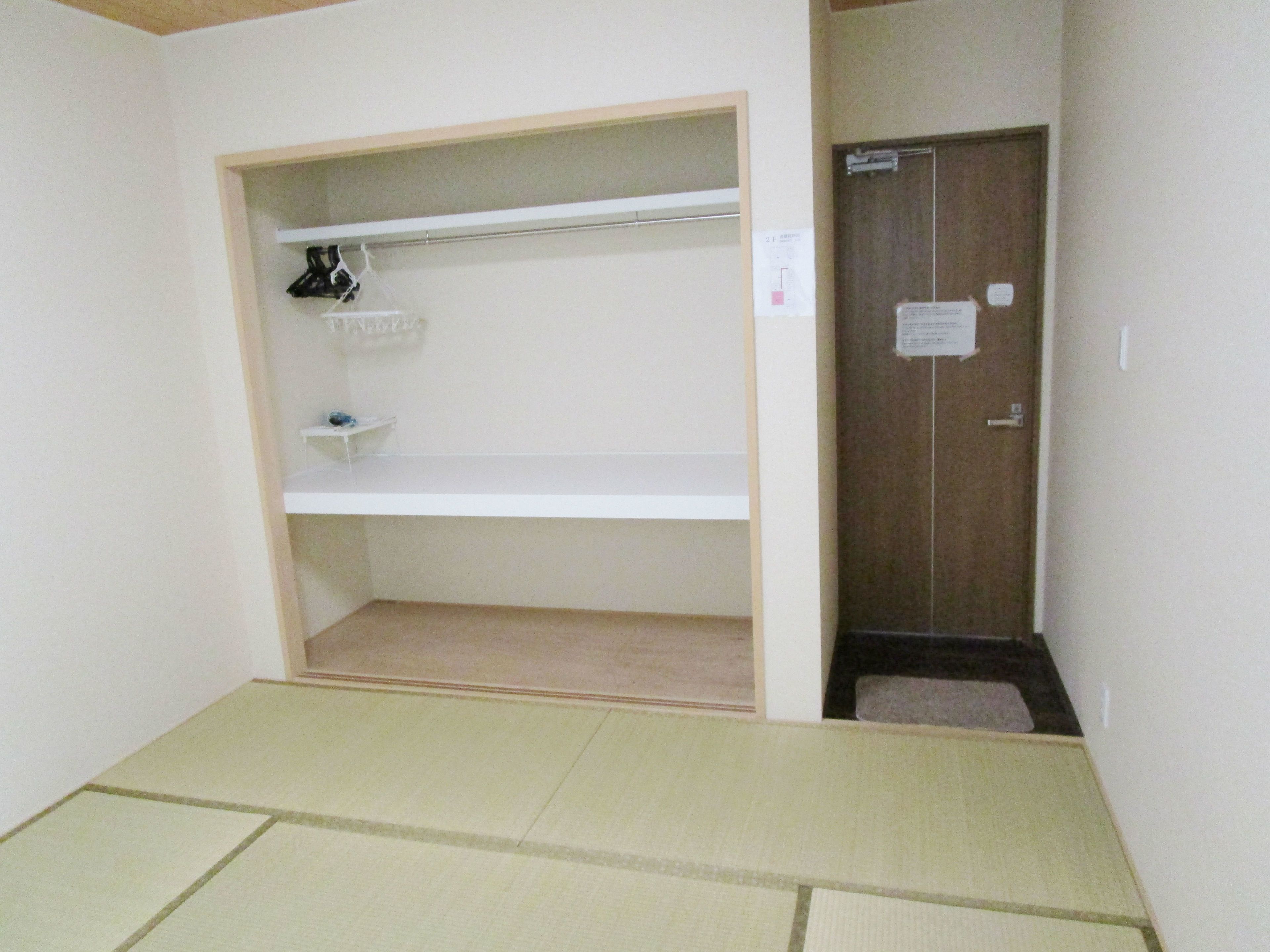 A room with a tatami mat floor, a wardrobe, and a shelf with a black item.