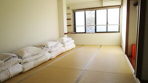 Een kamer met tatami matten, een futonbed, een raam met zonwering en een klein rode kastje.