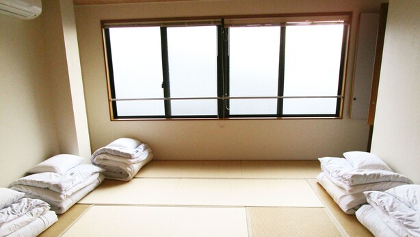 Een kamer met tatami matten, een groot raam en netjes opgemaakt bed.