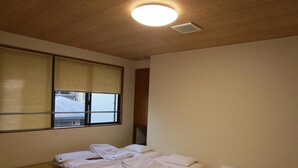 Een kamer met drie bedden langs de muur, een raam met jaloezieën en een plafondlamp.