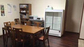 Een eetgedeelte met een houten tafel en stoelen, een boekenkast en een witte koelkast.