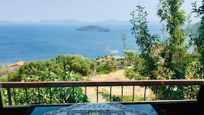 Una mesa con mantel de encaje y una vela, con vistas a un paisaje costero con árboles y una isla distante.