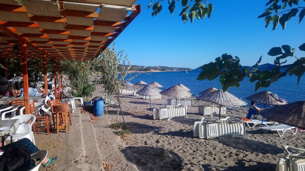 Un café frente a la playa con mesas al aire libre, sombrillas y vistas al mar.