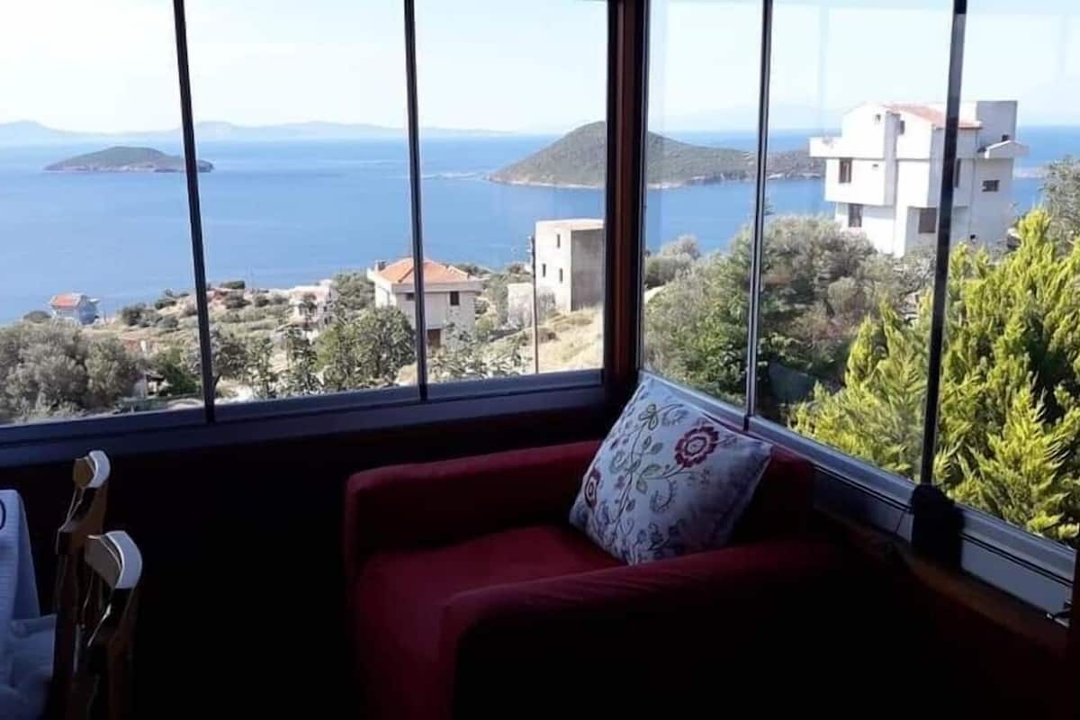 A room with a large window offering a view of the sea and distant hills.