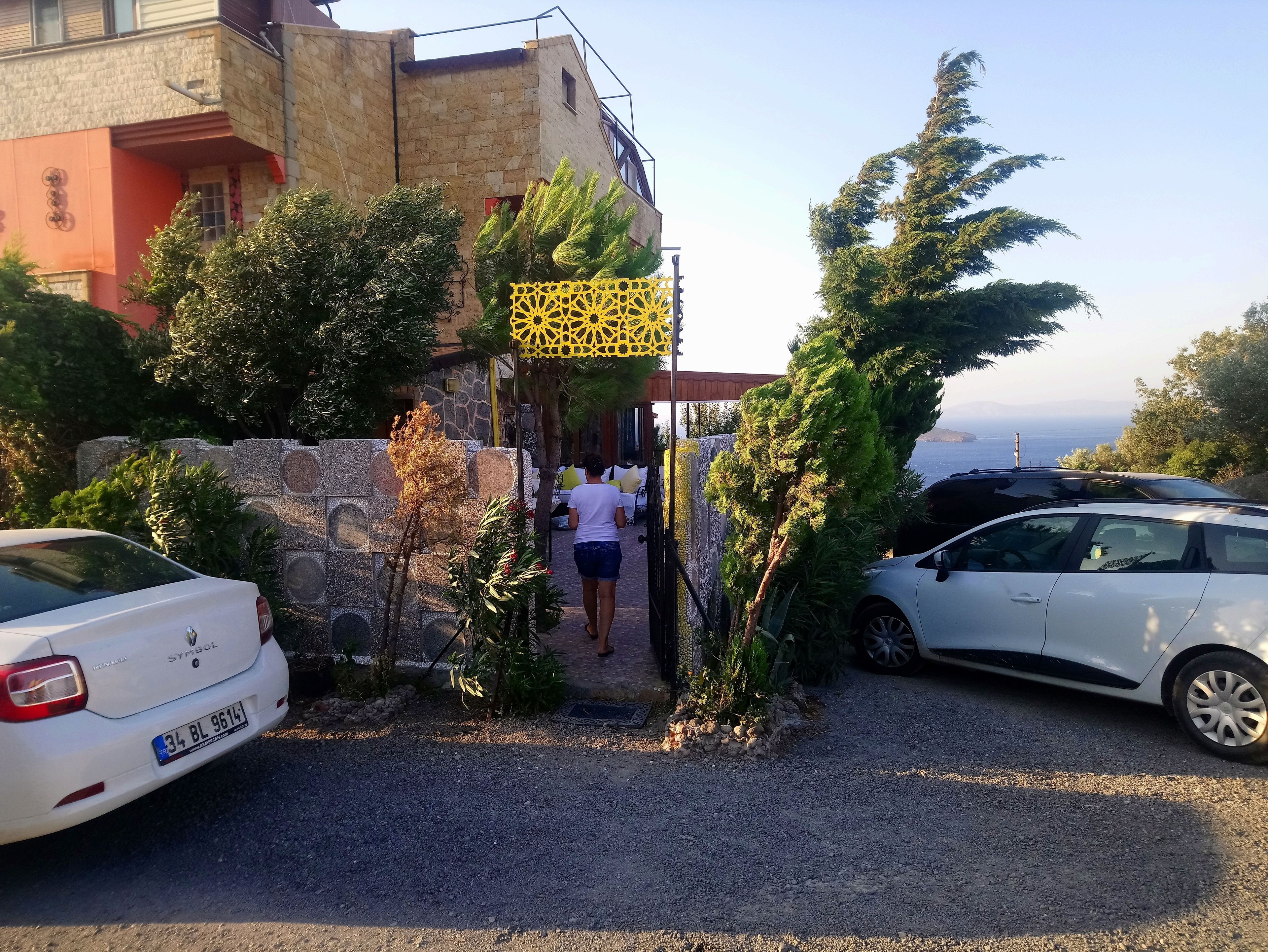 A parking area with two cars, a stone wall, and a building with a red facade.