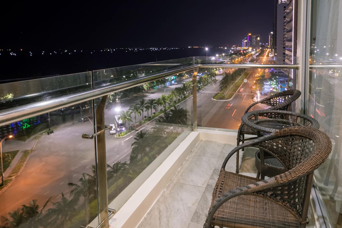 Un balcon avec des fauteuils en osier, une rambarde en verre et une vue sur le paysage urbain illuminé la nuit.