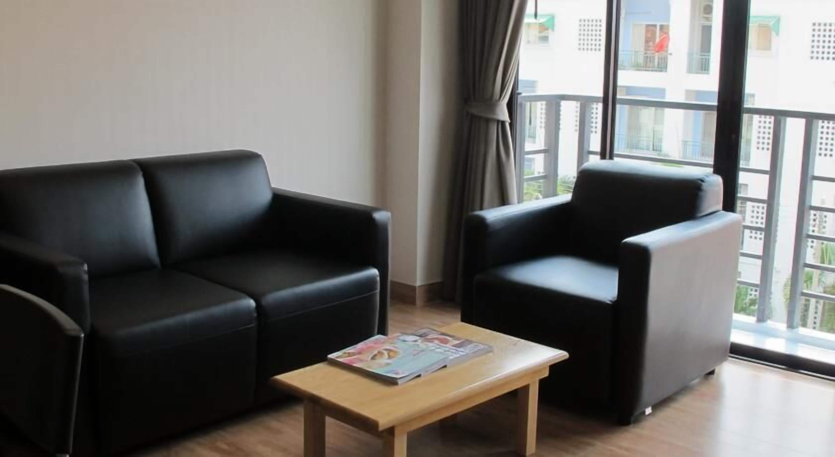 A modern living room with a black leather sofa, a matching armchair, and a wooden coffee table with a magazine.