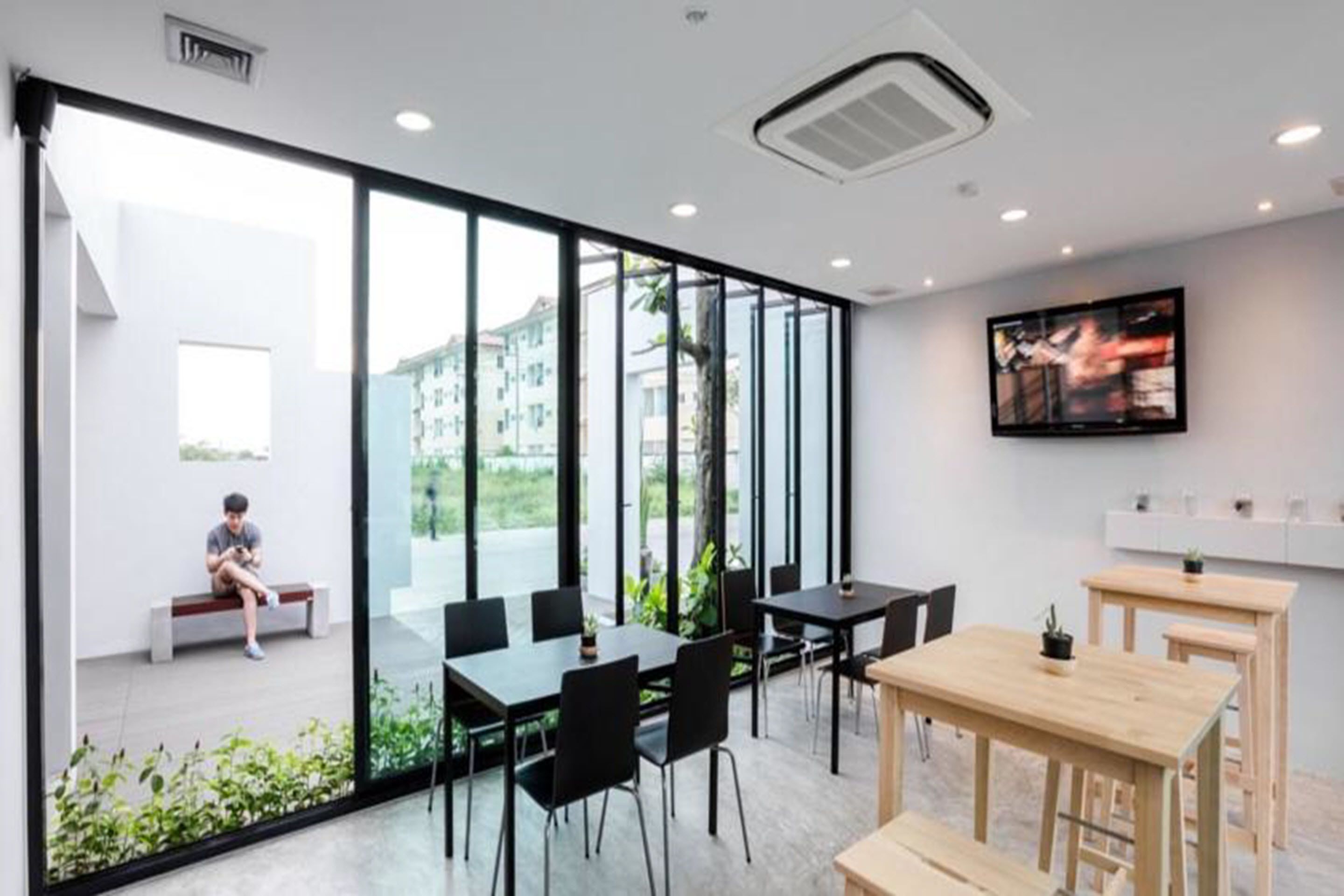 Uma sala de conferências moderna com paredes de vidro, uma televisão grande e uma área de estar com um banco.