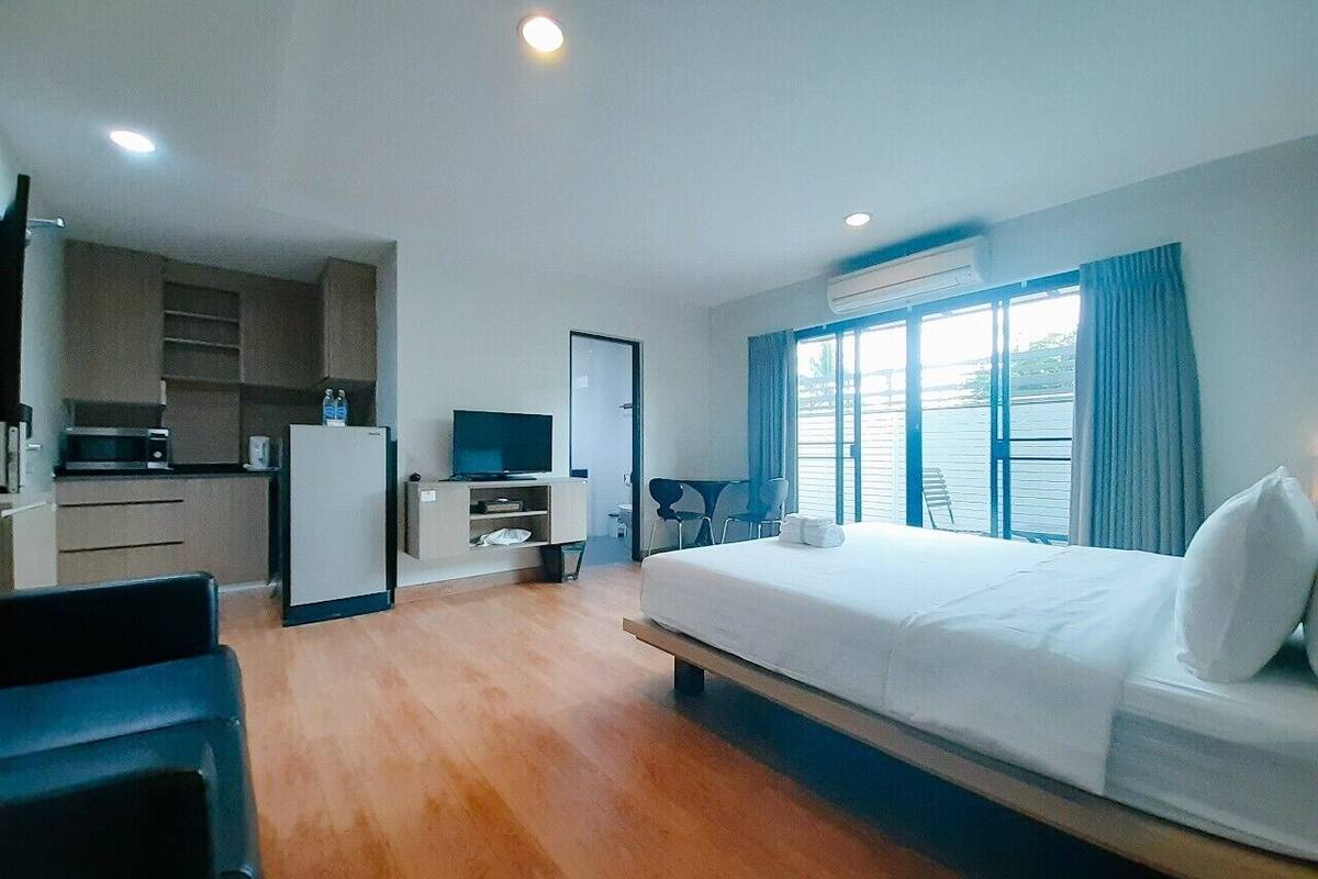A hotel room with a bed, a desk, a chair, a television, a kitchenette, and a window with curtains.