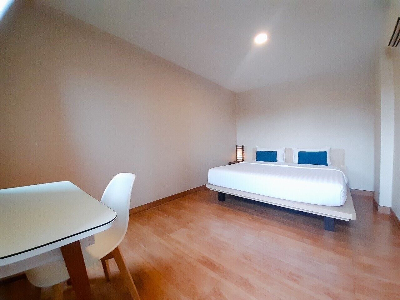 A small, modern room with a single bed, a white table, and a white chair.