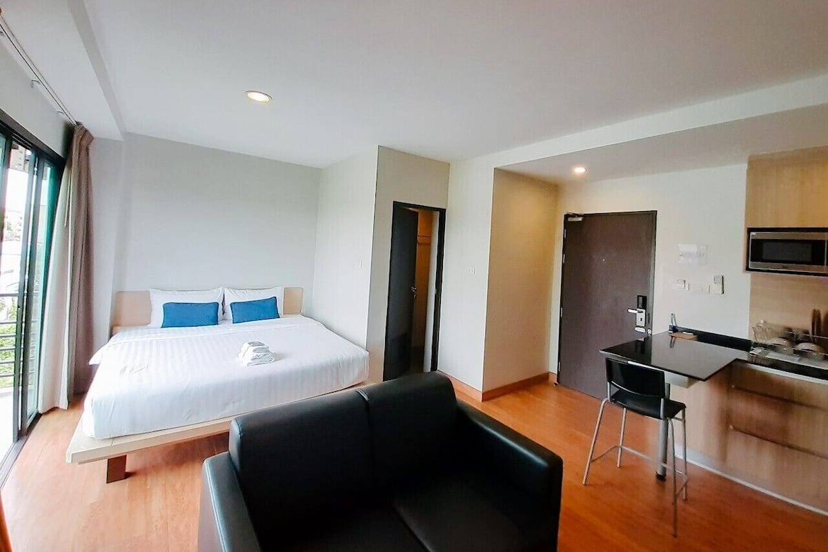 A modern hotel room with a large bed, a desk, and a kitchenette.