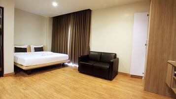 A hotel room with a bed, a black leather sofa, wooden flooring, and a wardrobe.