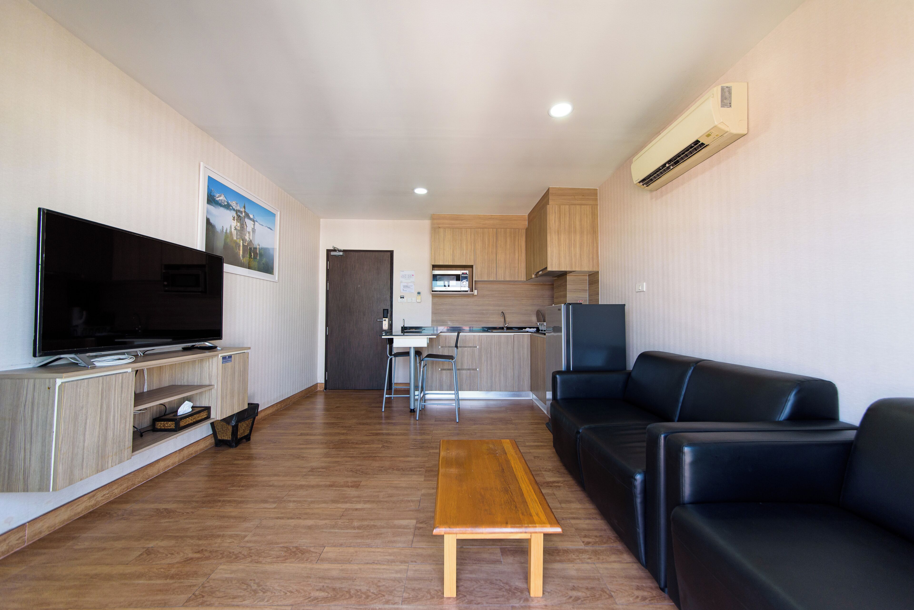 Ein modernes Wohnzimmer mit Flachbildfernseher, Couchtisch aus Holz, einer schwarzen Ledersofa und einer Küchenzeile im Hintergrund.