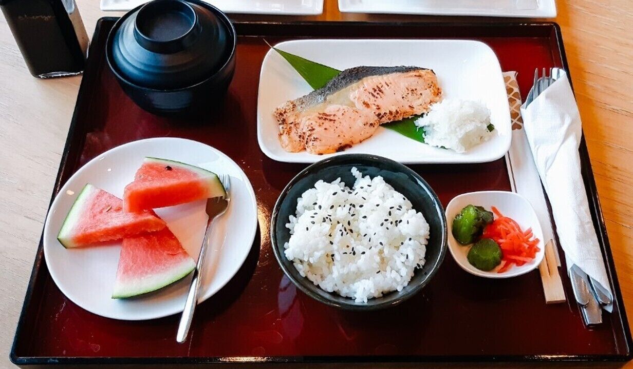 A tray with a salmon fillet, rice, watermelon slices, and a small dish of vegetables.