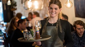 A person holding a tray with glasses and a bottle, in a dimly lit indoor setting with hanging lights. - Wolf Hotel Kitchen & Bar (Alkmaar)