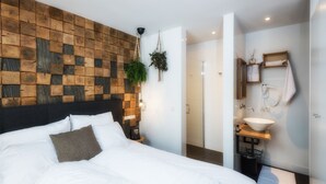 A modern hotel room with a wooden headboard, a large bed with white linens, a bedside table with a lamp, and a bathroom with a wooden vanity and a large sink. - Wolf Hotel Kitchen & Bar (Alkmaar)