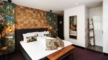 A bedroom with a large bed, a wooden headboard, a bench, a mirror, and a bathroom with a towel rack and a ladder.