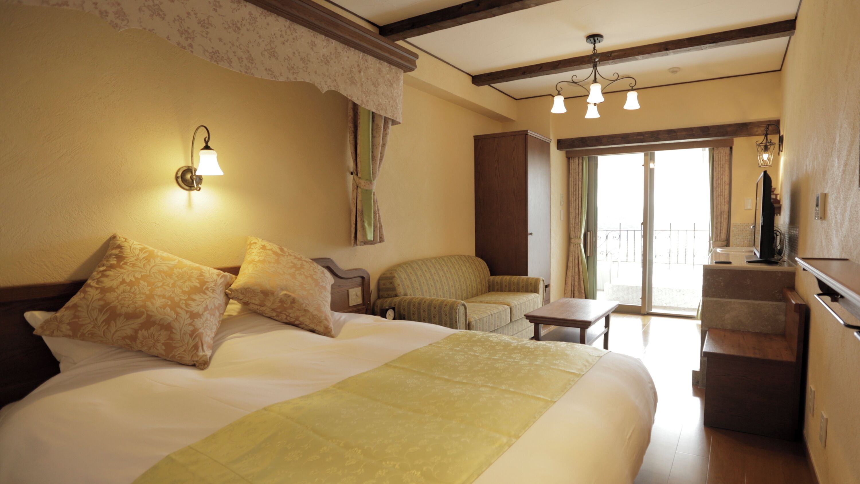 Quarto de hotel com uma cama, uma cadeira, uma mesinha, uma televisão e uma varanda.