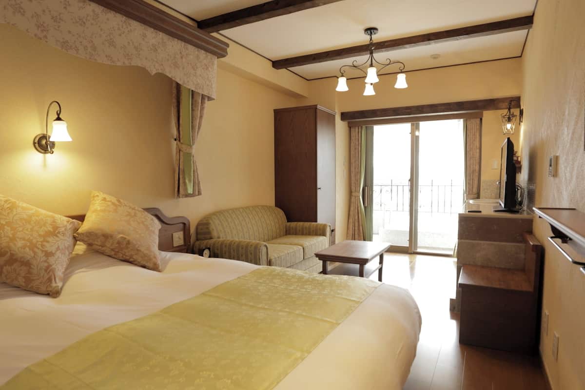 Quarto de hotel com uma cama, uma cadeira, uma mesinha, uma televisão e uma varanda.