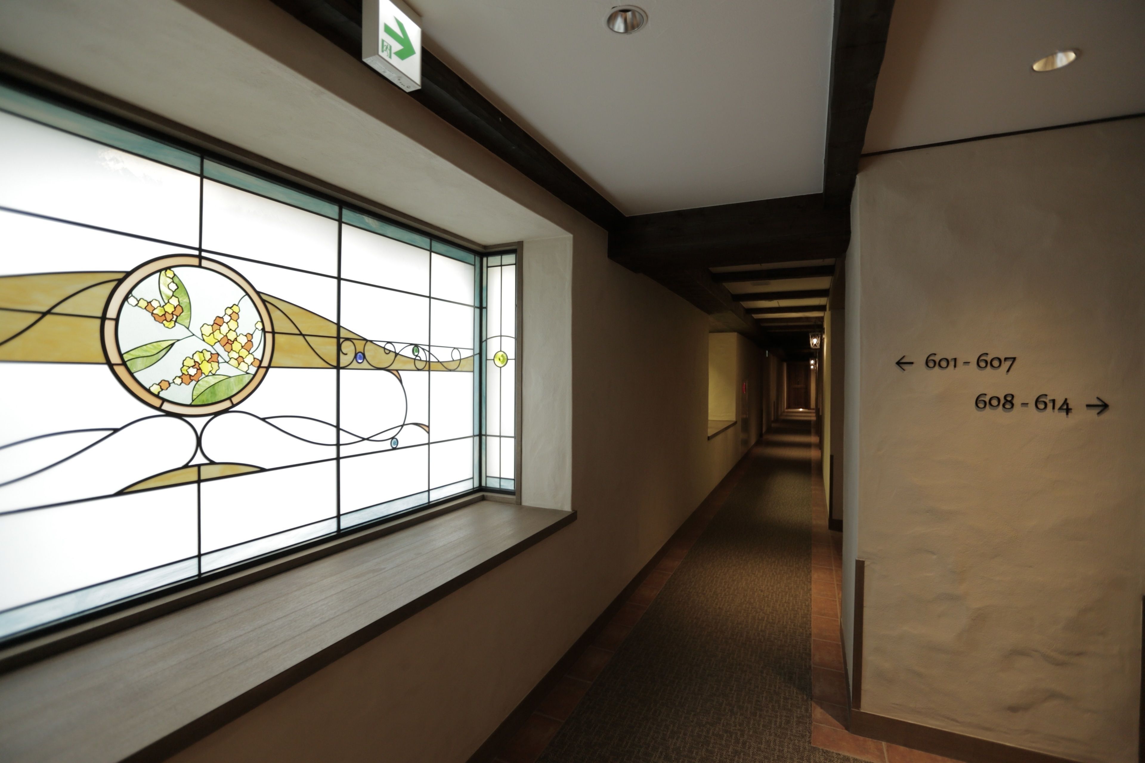 A hallway with a stained glass window, directional signs, and a carpeted floor.
