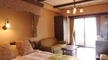 A hotel room with a bed, two chairs, a small table, a desk, a lamp, and a view of the outdoors.
