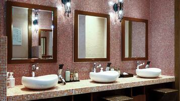 A bathroom with three sinks, two mirrors, and a tiled backsplash.