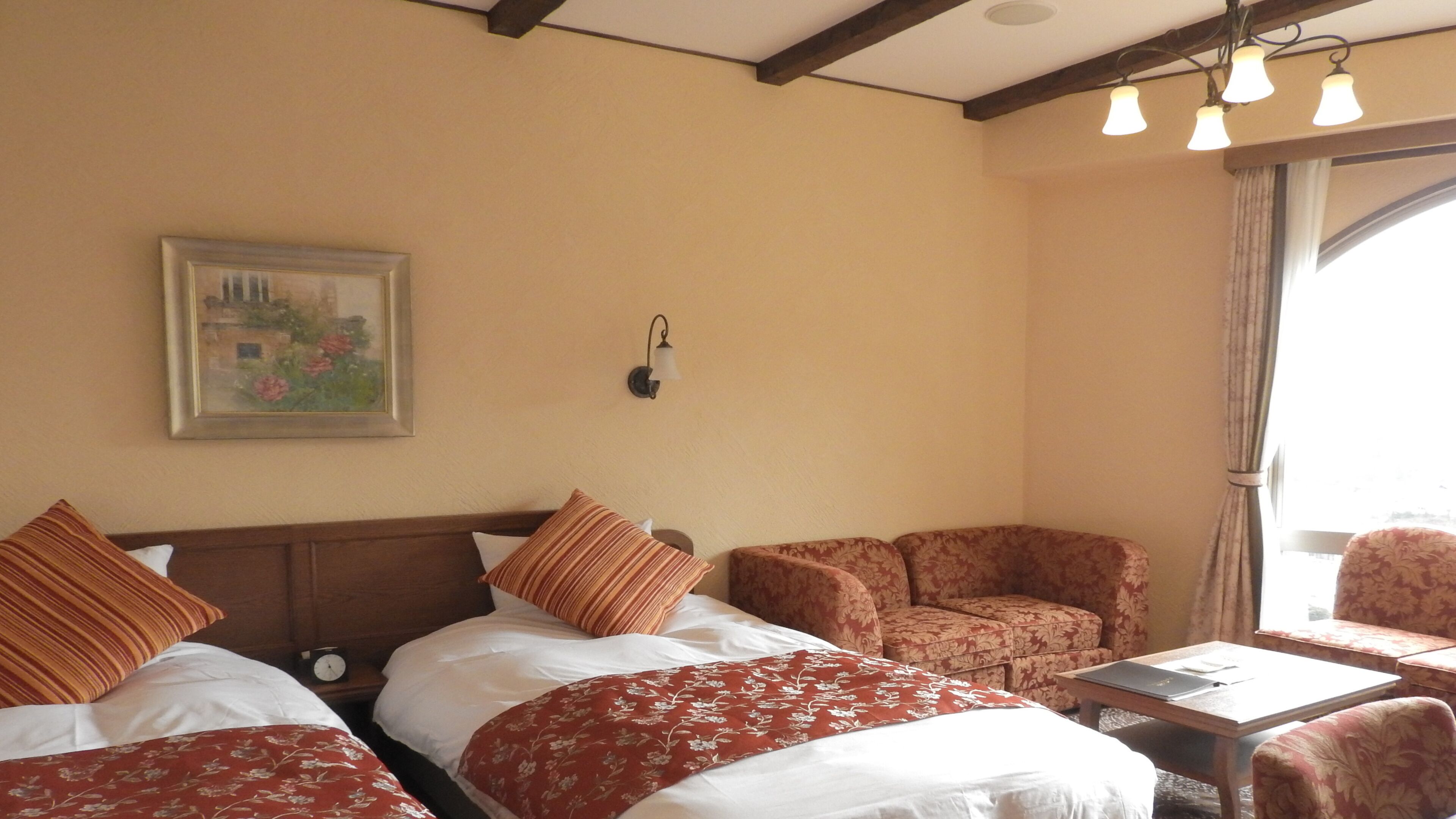 Quarto de hotel com duas camas, um sofá, uma mesa, um relógio, um quadro e uma janela com cortinas.