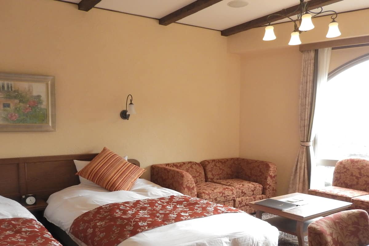 Quarto de hotel com duas camas, um sofá, uma mesa, um relógio, um quadro e uma janela com cortinas.