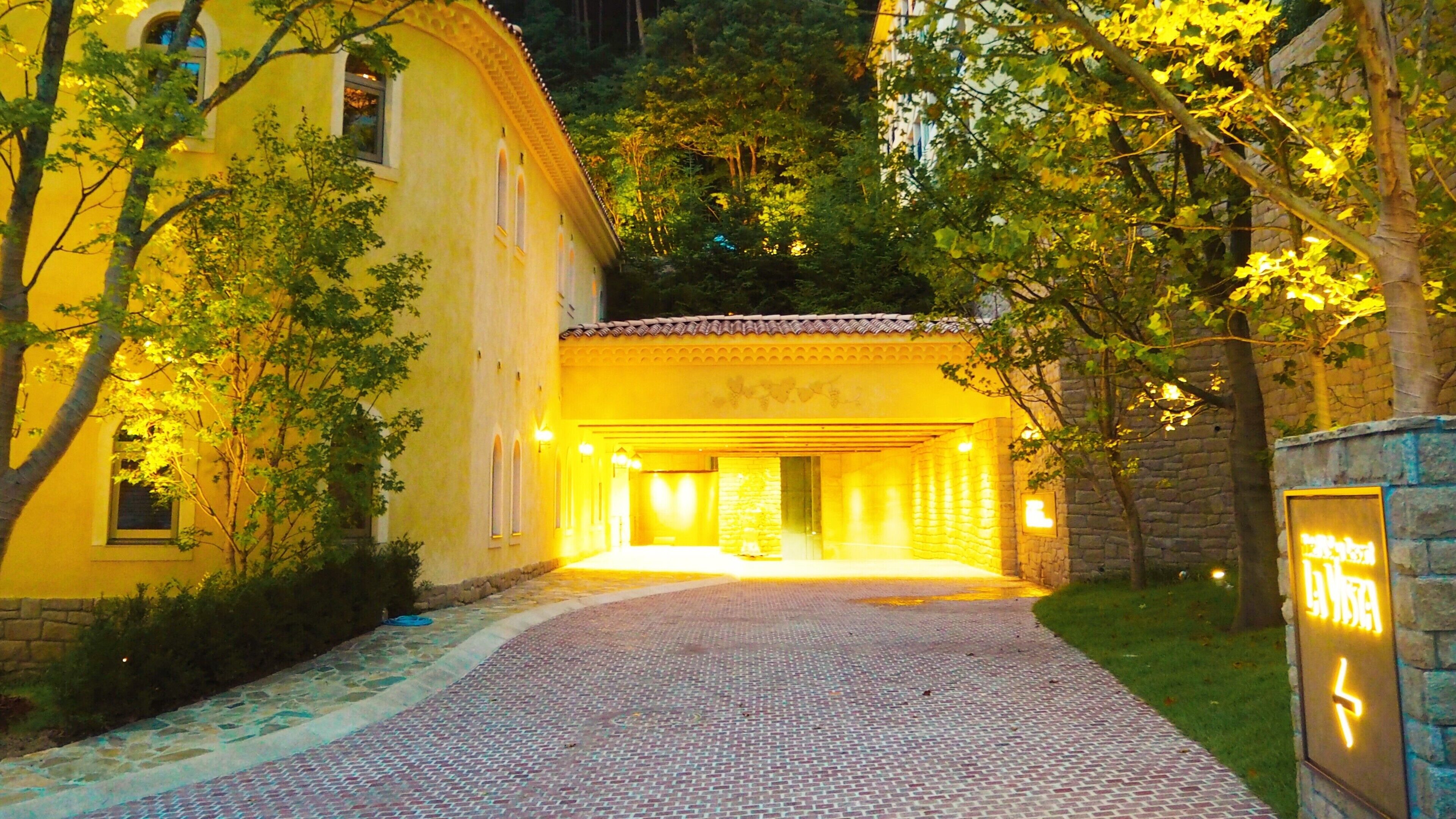 Um edifício com fachada amarela, entrada de pedra e um caminho pavimentado que leva até ele.