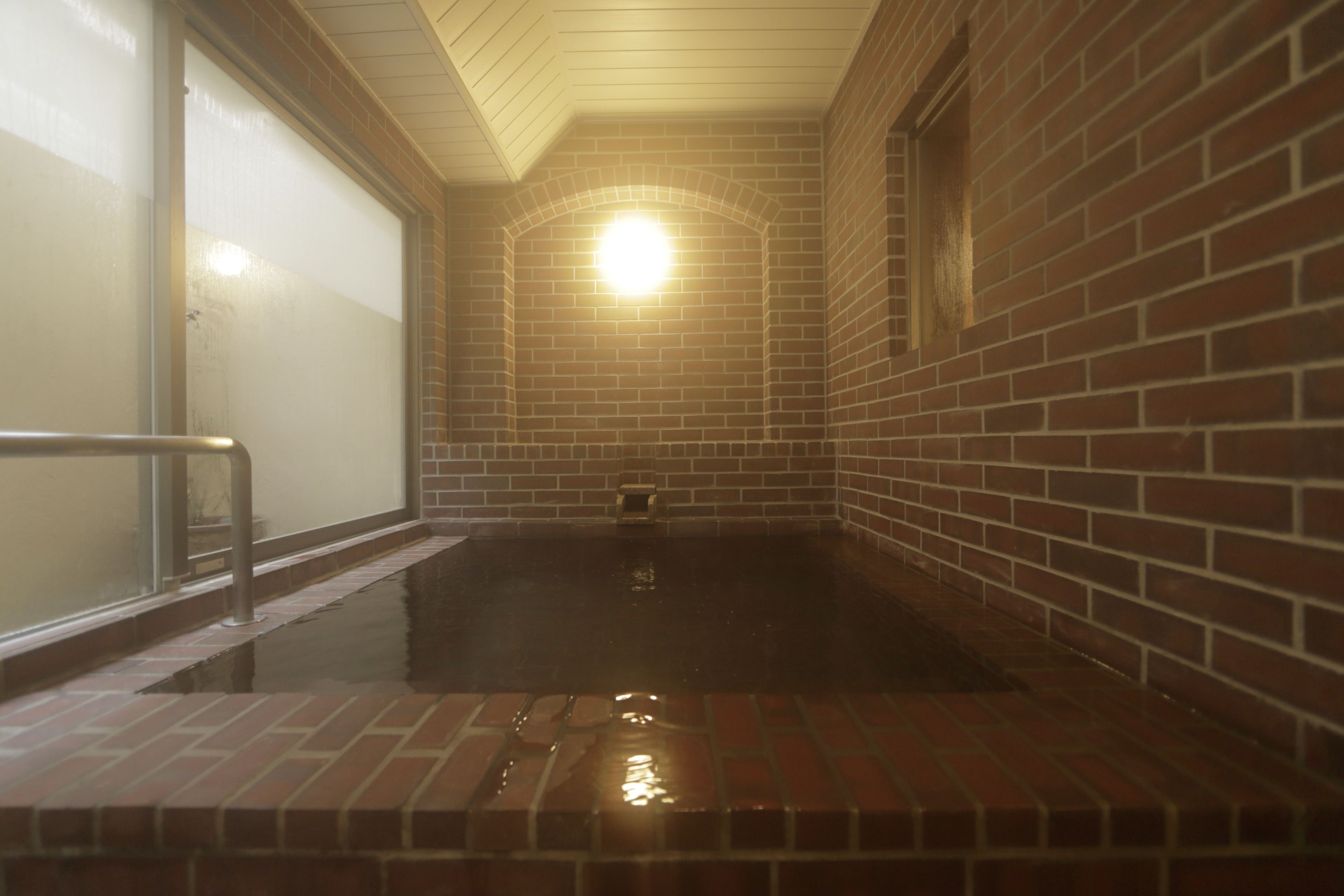 A hot tub area with a brick wall and a glass door.