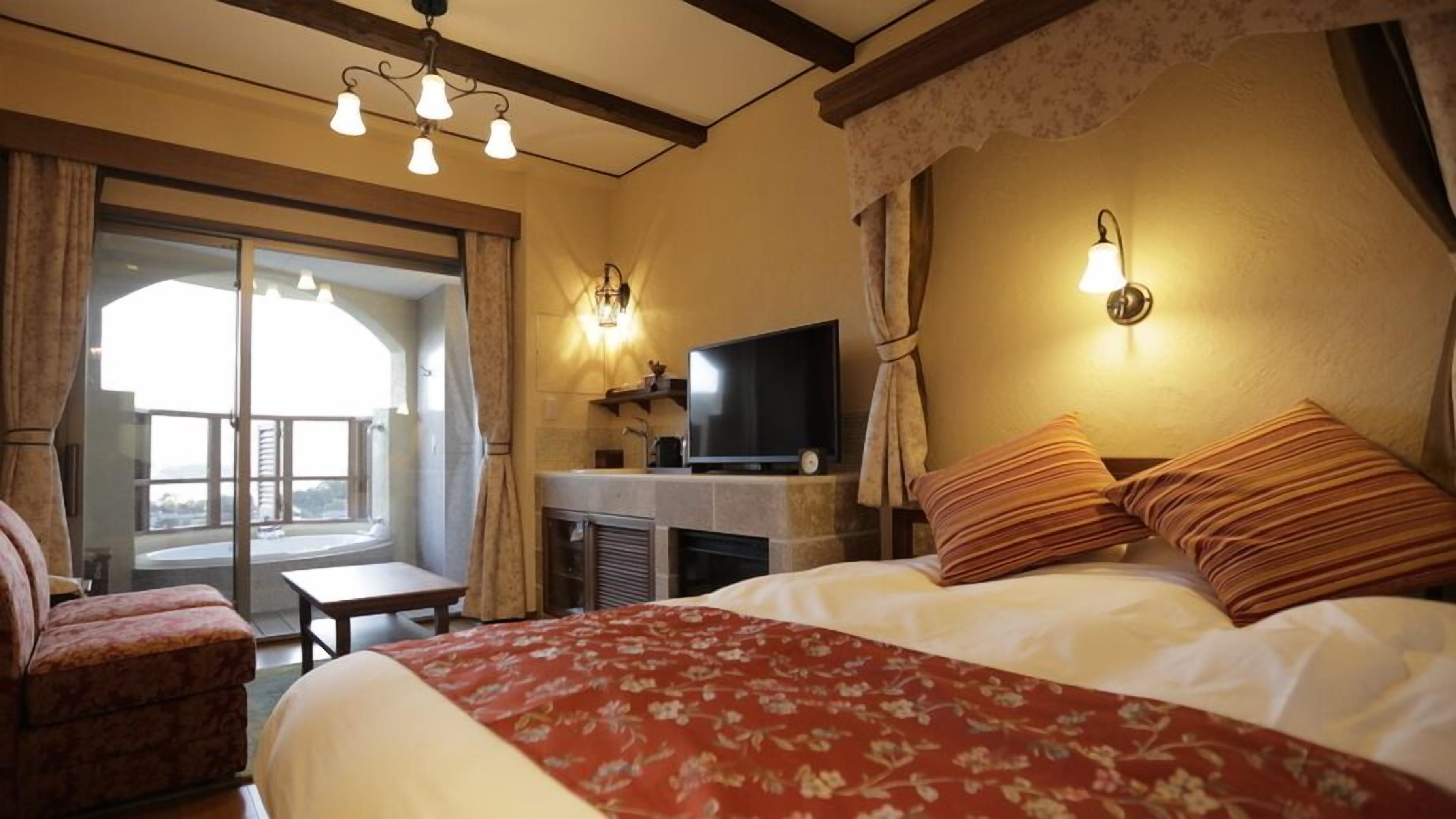 Quarto de hotel com cama, televisão, lareira e varanda com cortinas.