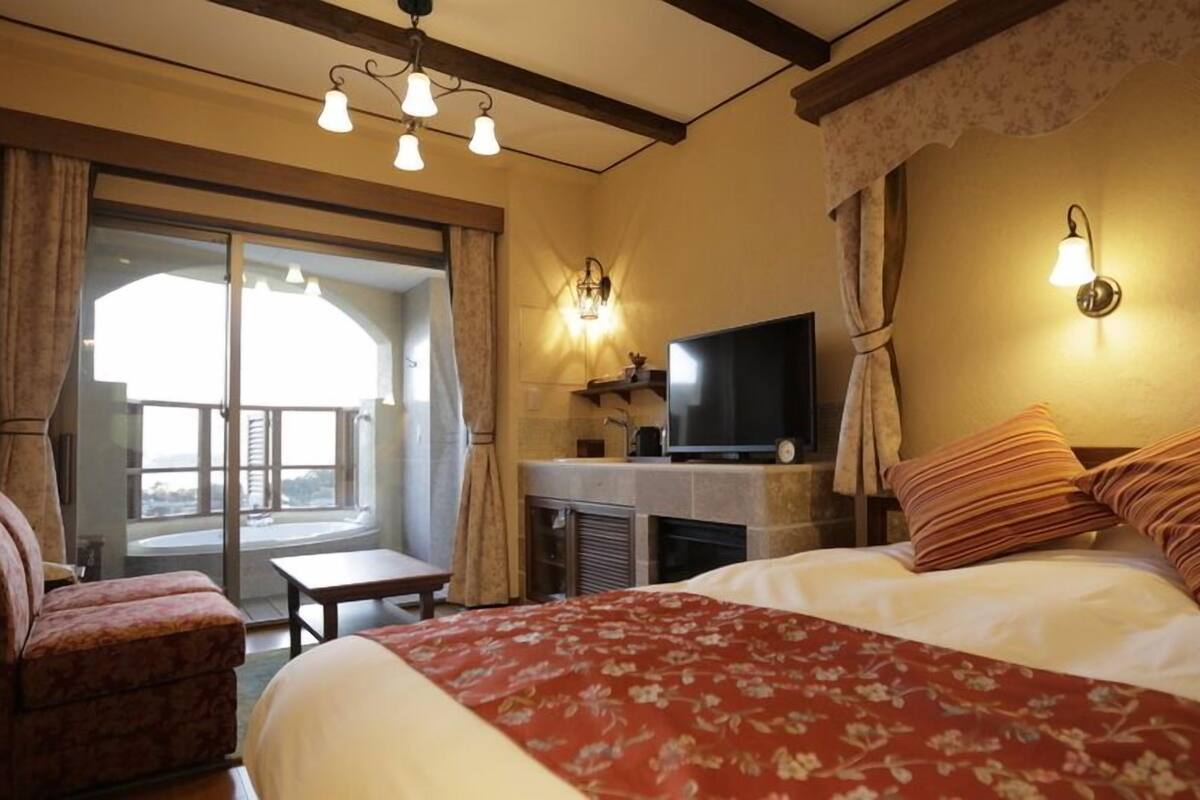 Quarto de hotel com cama, televisão, lareira e varanda com cortinas.