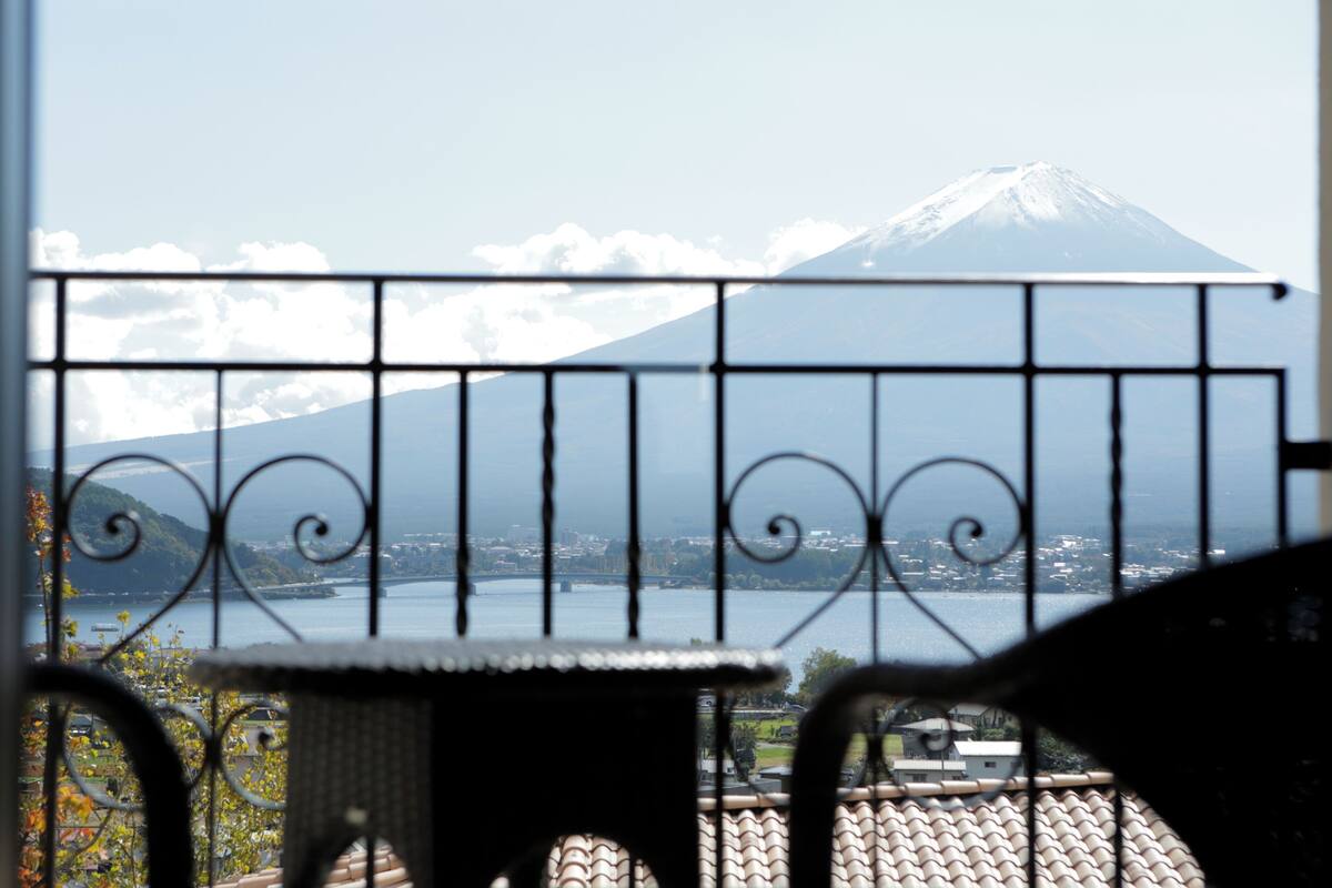 Un balcon doté d’une balustrade en métal, offrant une vue sur le paysage urbain et une montagne enneigée.