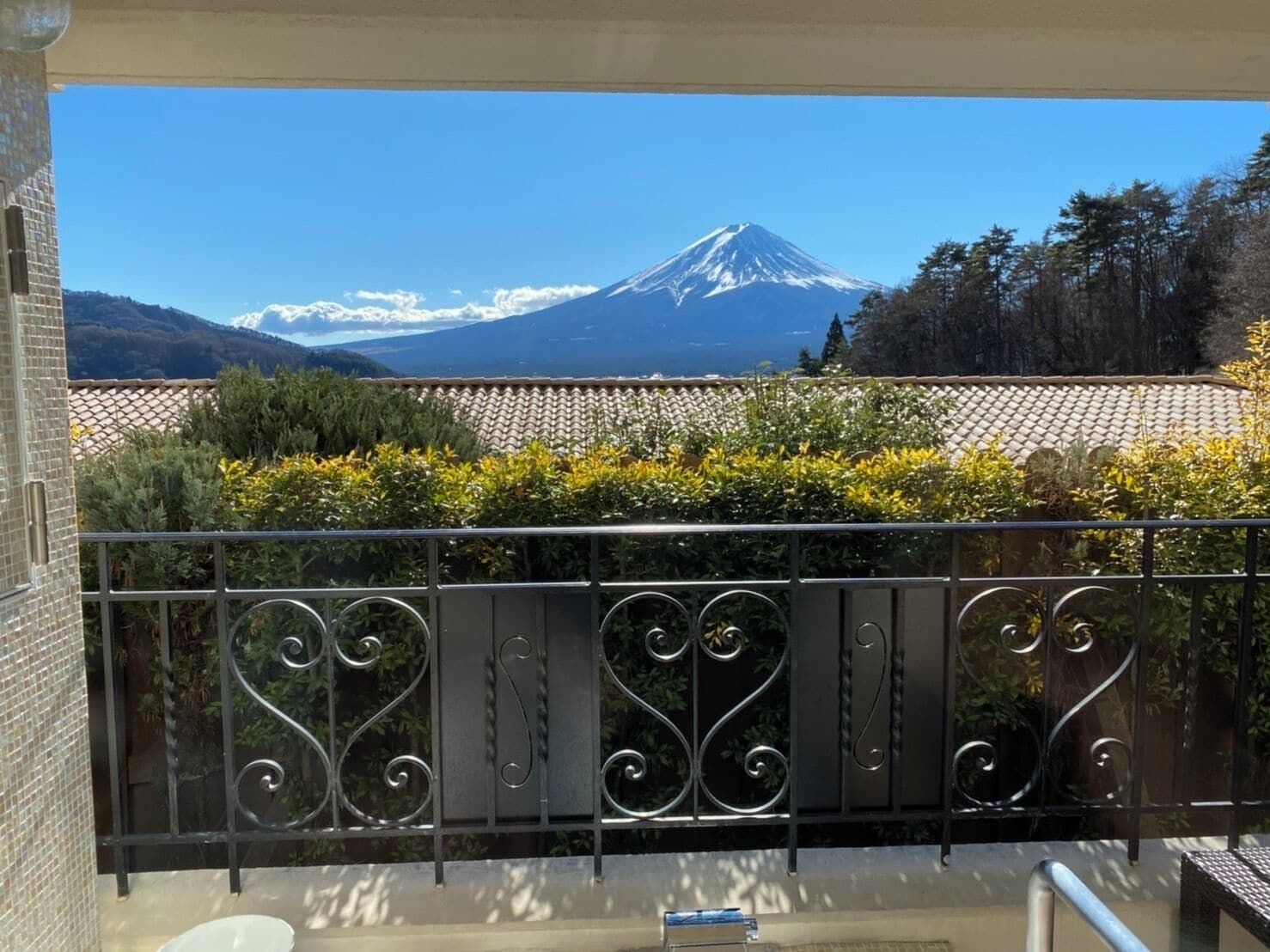 A balcony with a wrought iron railing, a view of a mountain, and a tiled roof in the background.