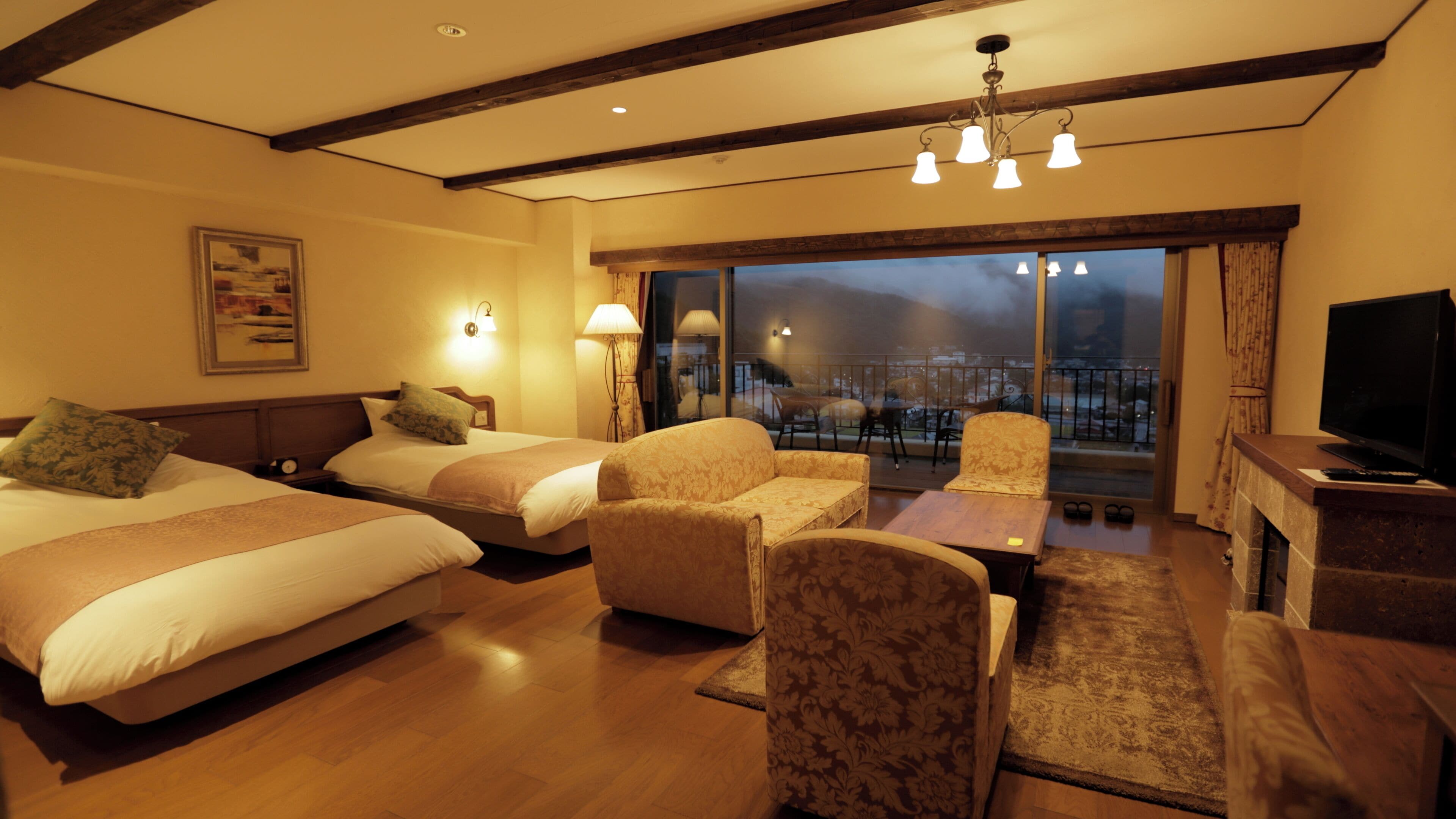 Quarto de hotel com duas camas, um sofá, uma TV e uma varanda com vista.