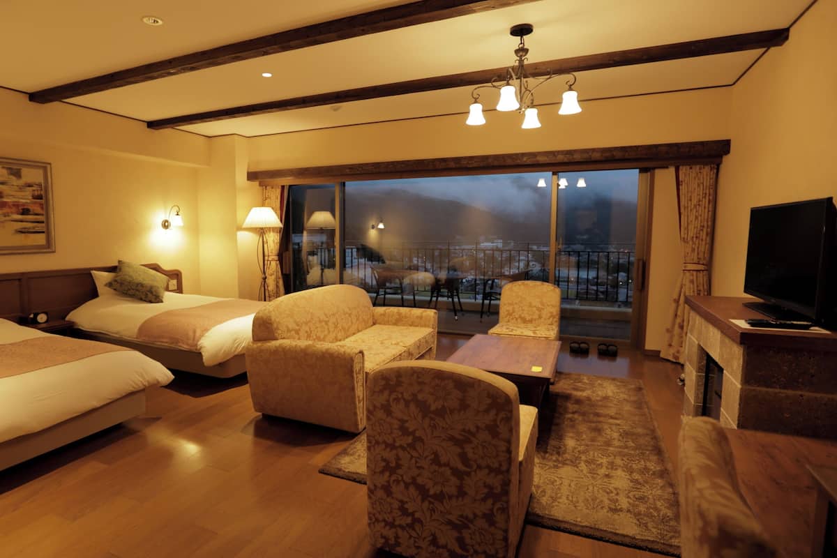 Quarto de hotel com duas camas, um sofá, uma TV e uma varanda com vista.