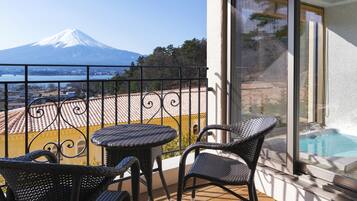 Un balcon avec des fauteuils en osier et une table, offrant une vue sur une piscine et sur les montagnes.