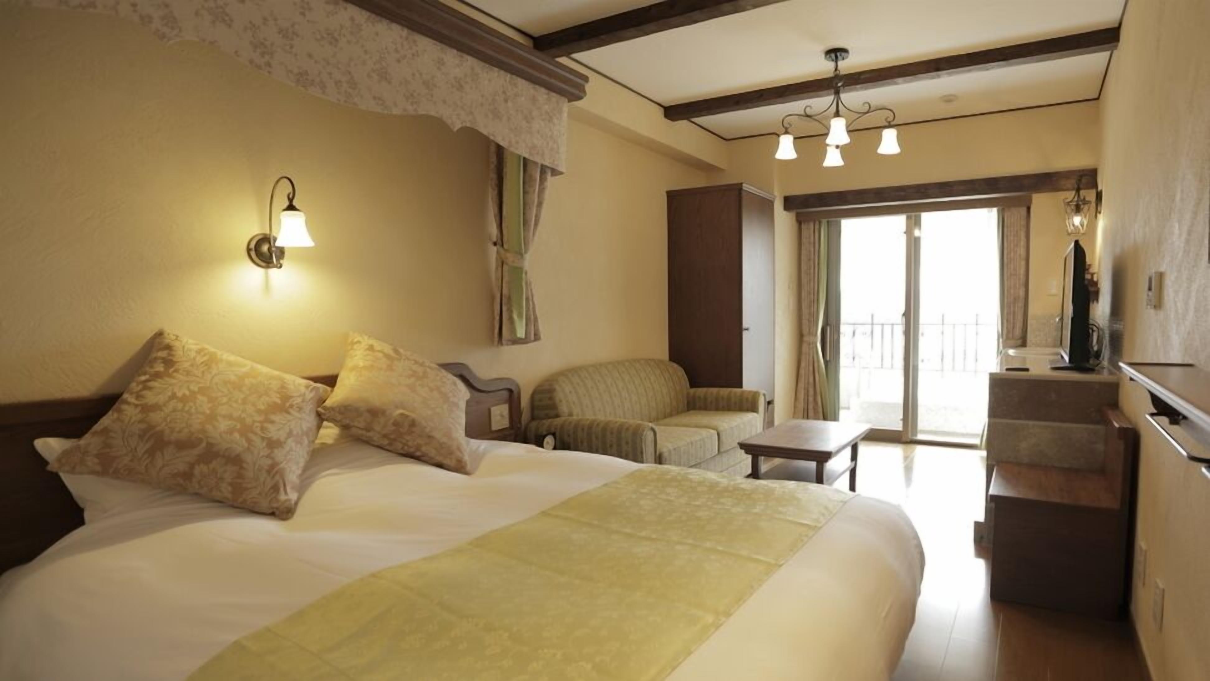 Quarto de hotel com cama grande, uma cadeira, mesinha e varanda com vista.
