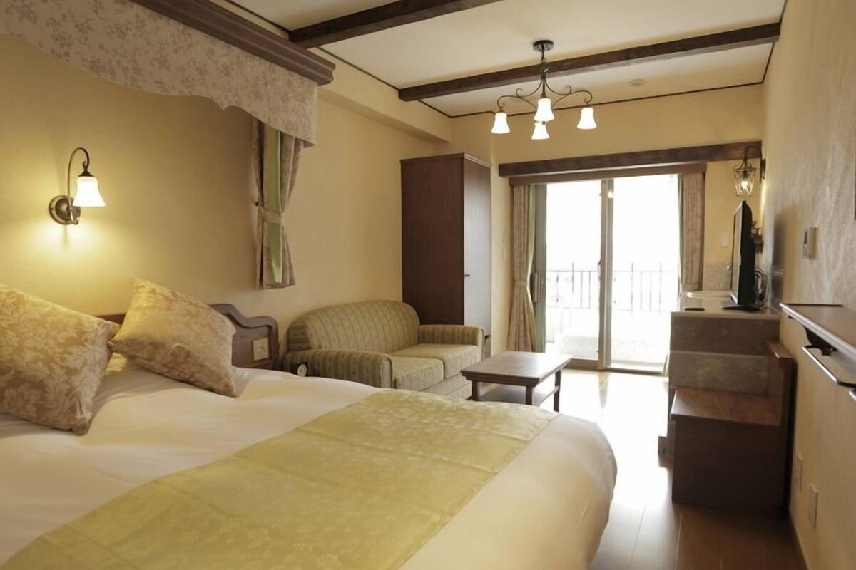 Quarto de hotel com cama grande, uma cadeira, mesinha e varanda com vista.