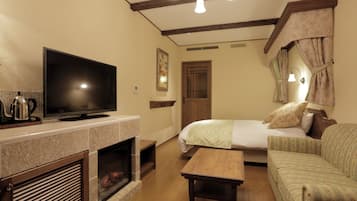 Una habitación acogedora con televisión sobre una repisa, una cama con manta verde, una mesa de madera y una chimenea.