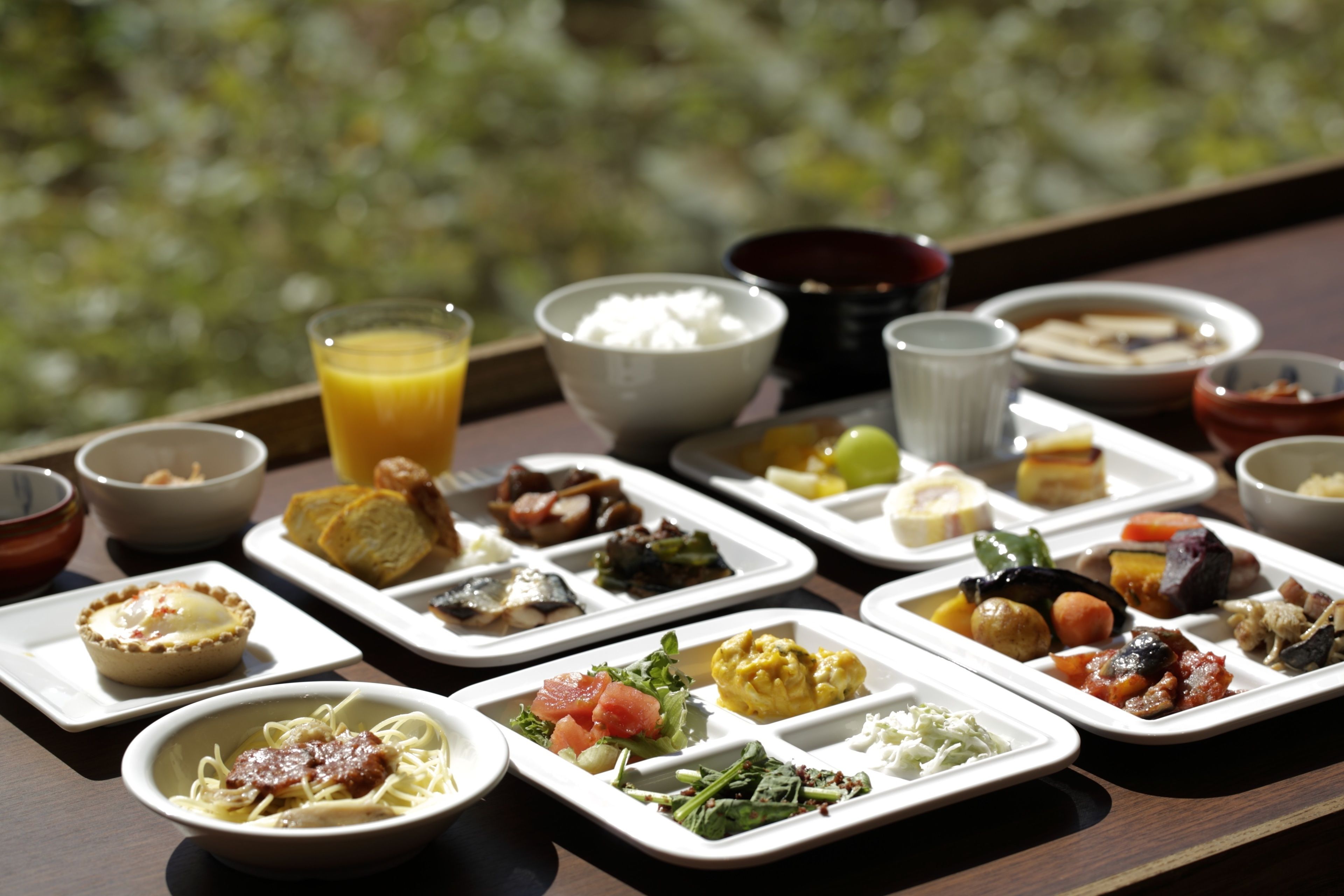 A variety of dishes arranged on a table with a view of greenery in the background.