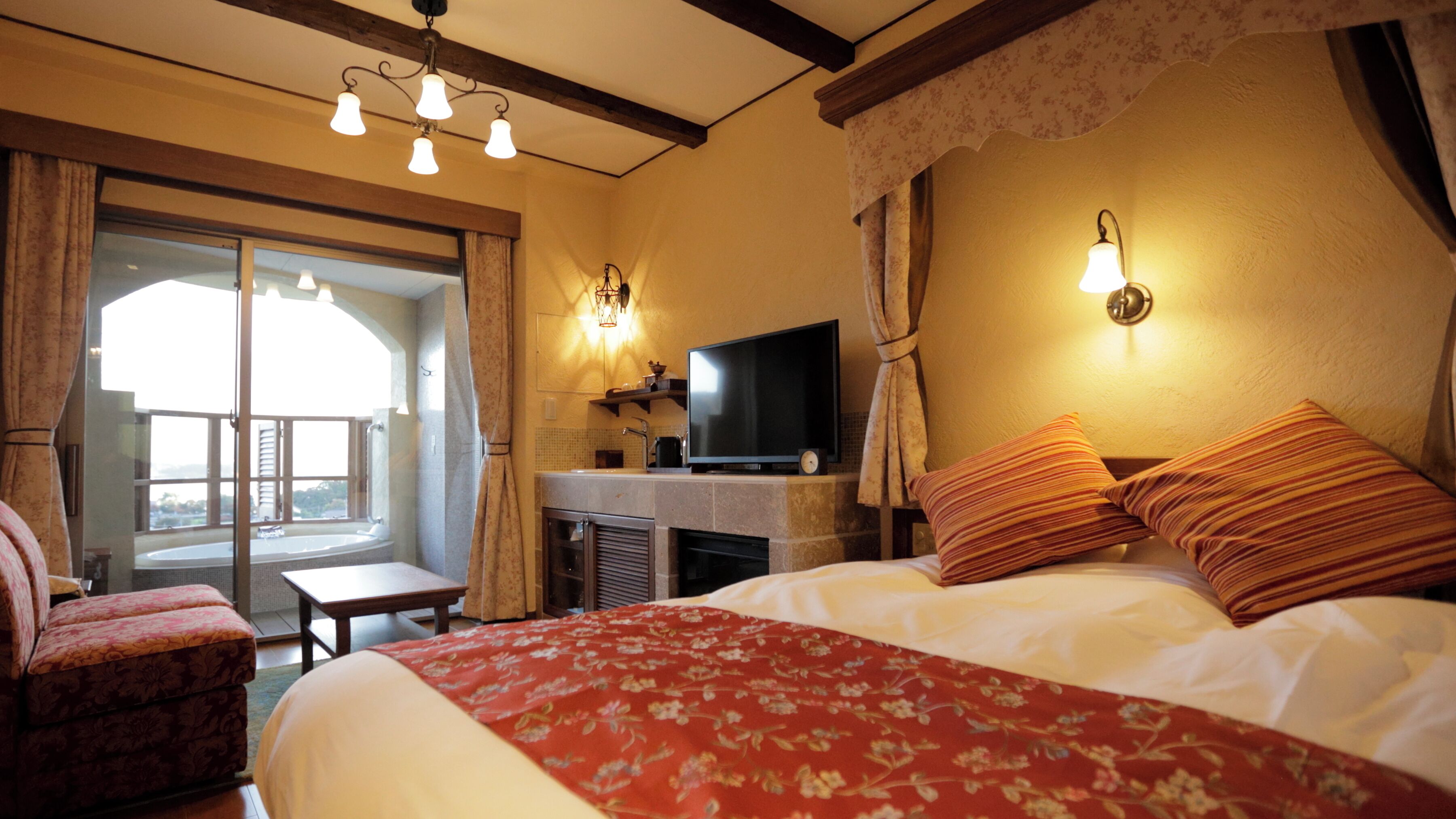 Quarto de hotel com cama, escrivaninha com televisão, cadeira e varanda.