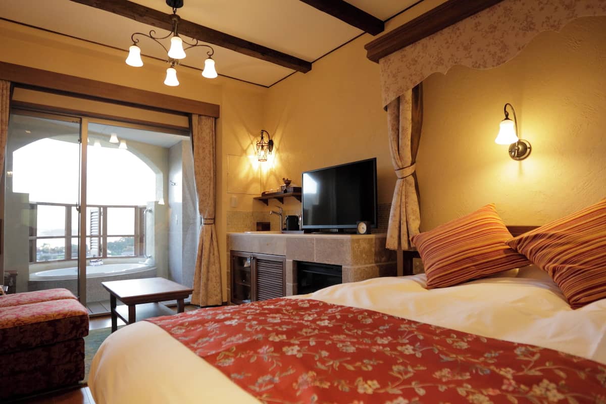 Quarto de hotel com cama, escrivaninha com televisão, cadeira e varanda.