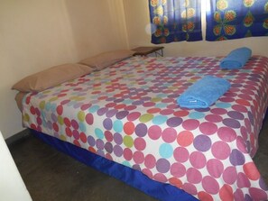 Un lit avec une couvre-lit à pois colorés, un oreiller marron et une serviette bleue posée dessus.
