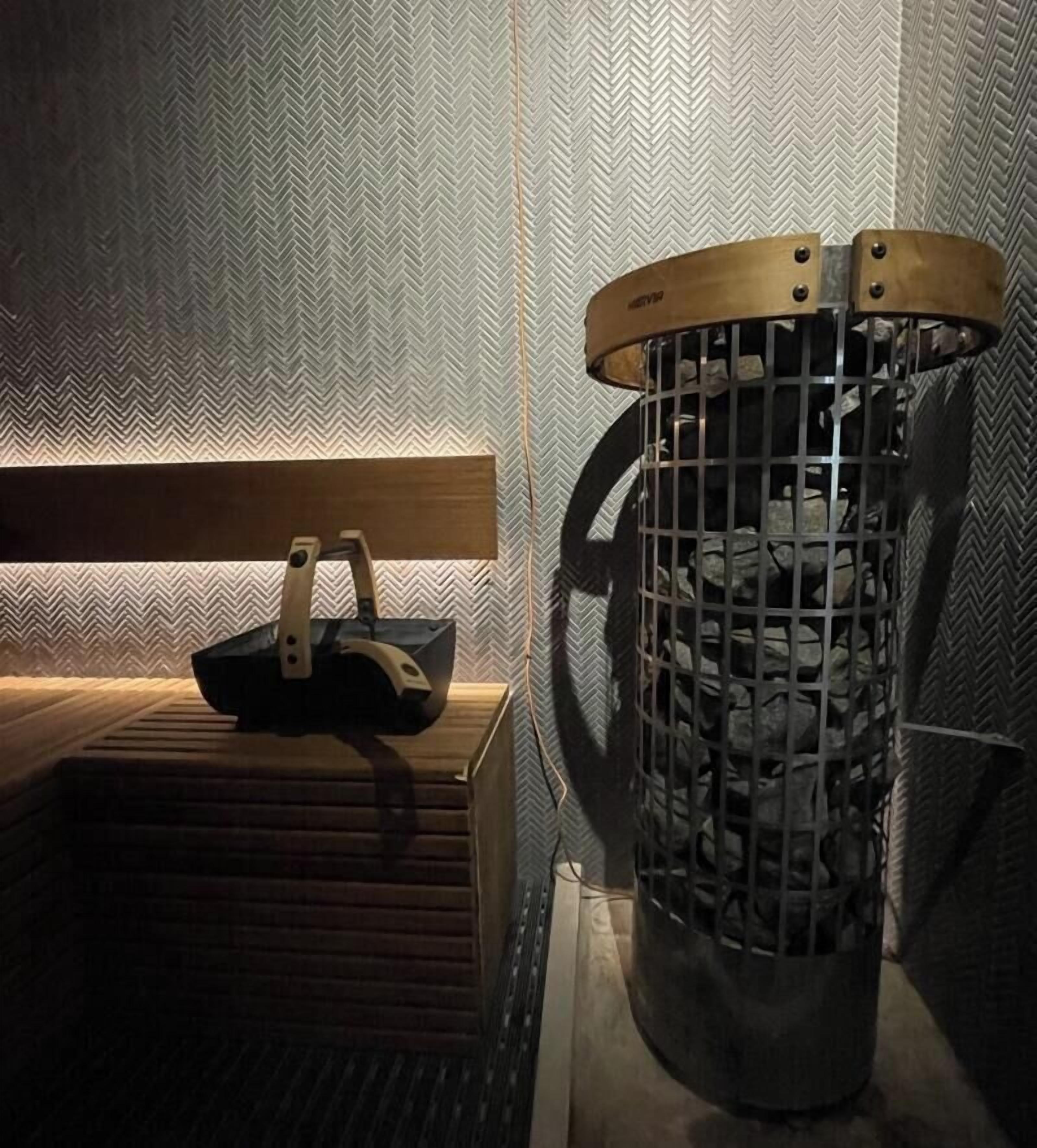 A room with a herringbone-patterned wall, a wooden bench, and a metal trash bin.