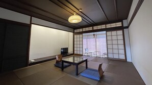 Una habitación tradicional japonesa con suelo de tatami, una mesa baja, una silla y un televisor.
