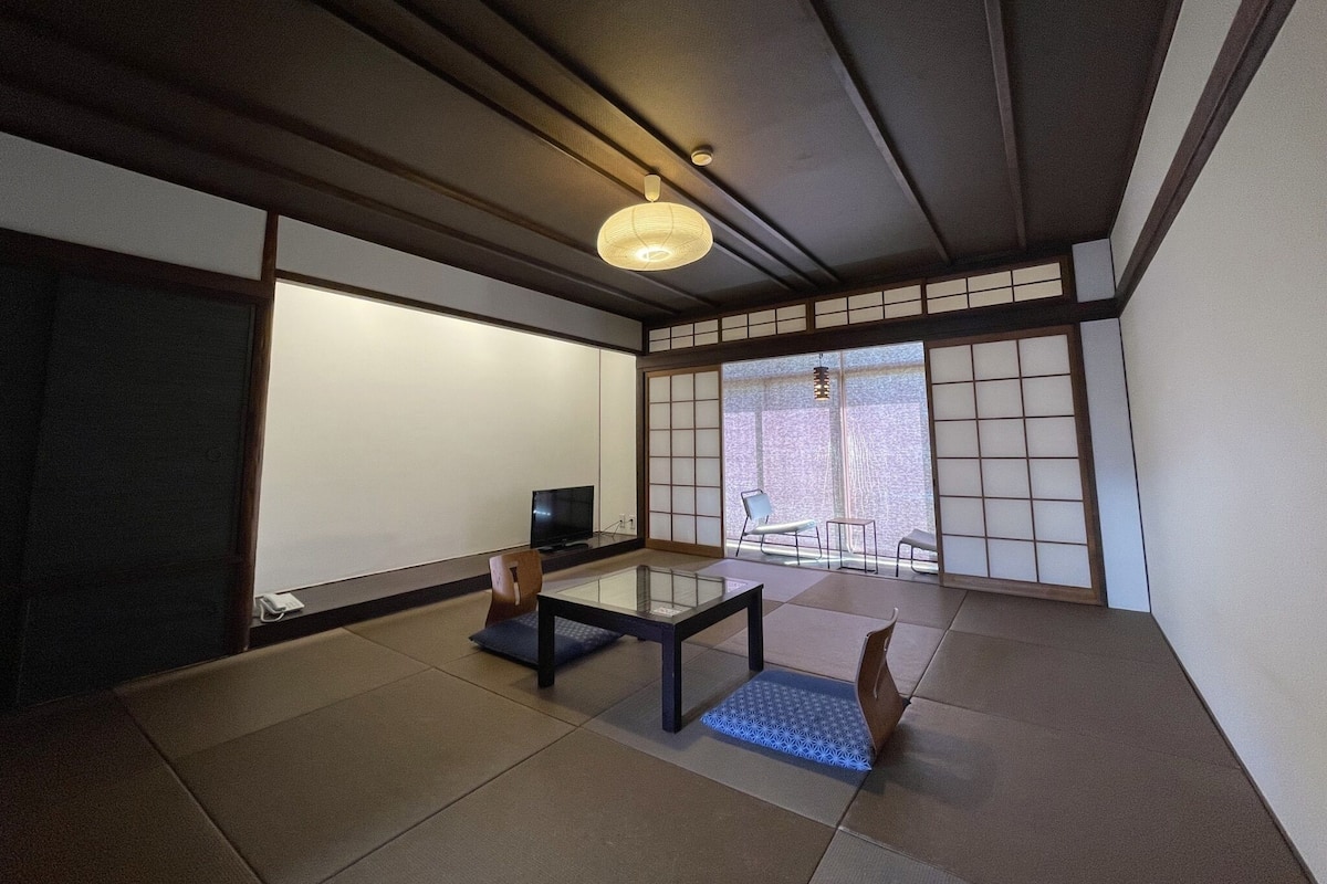 A traditional Japanese room with tatami flooring, a low table, a chair, and a television.