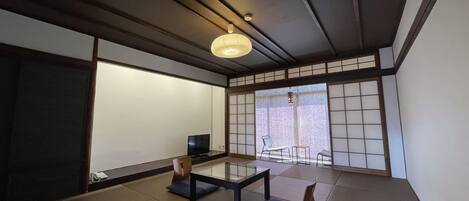 Une pièce de style japonais traditionnel, avec un sol recouvert de tatamis, une table basse, une chaise et un téléviseur.