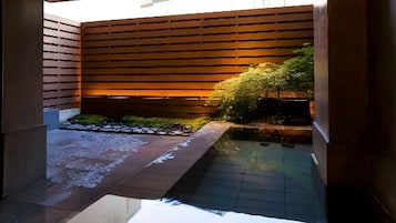 Un espacio exterior moderno con cerramiento de madera, una fuente pequeña y suelo de baldosas.
