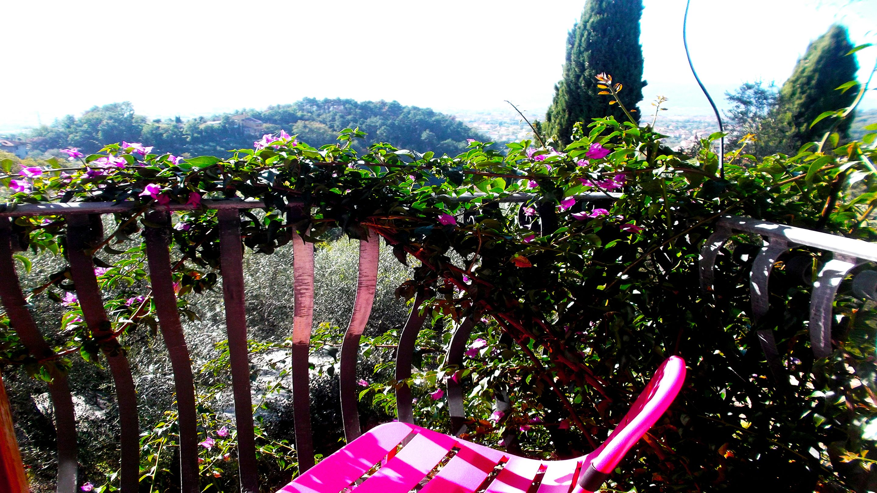 A balcony with a metal railing, a pink chair, and a view of a hilly landscape.